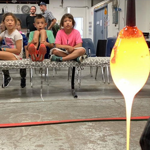 image of intensely engaged children watching a glass blowing demonstration with intensely hot glass dripping from a metal rod