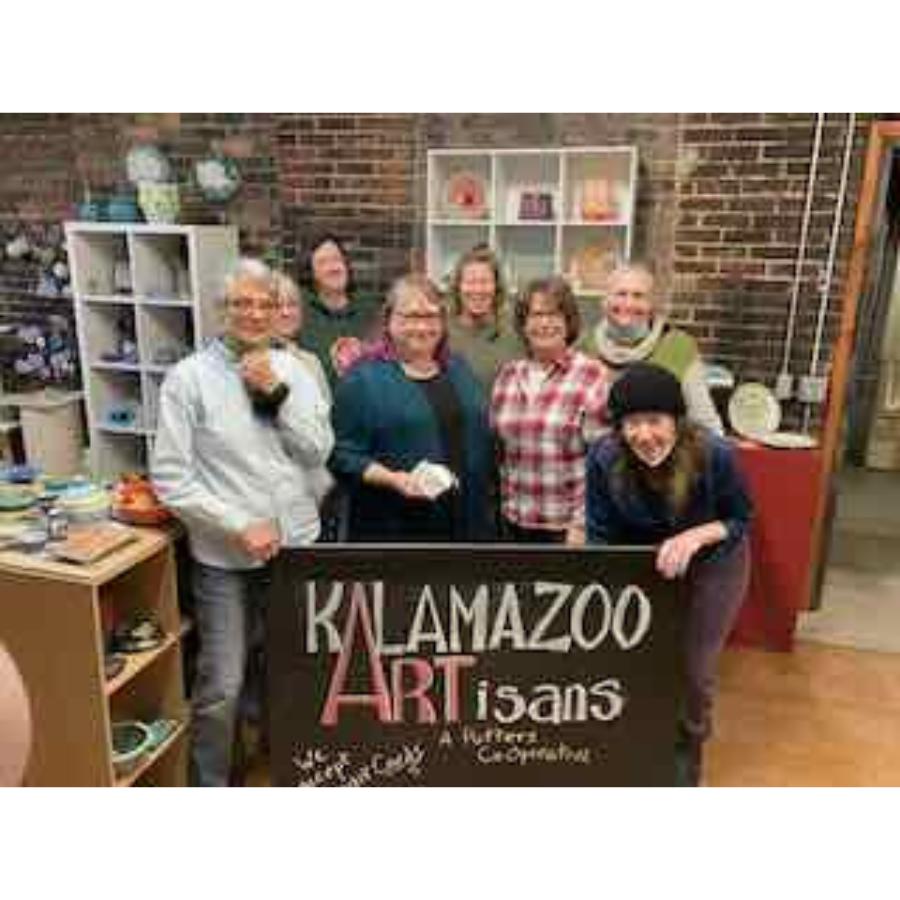 Group photo of people in an art studio/shop in front of a sign that says "Kalamazoo ARTisans"