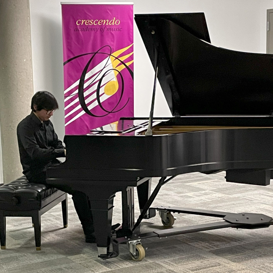 A person playing a grand piano with a purple banner behind him with the Crescendo logo on it