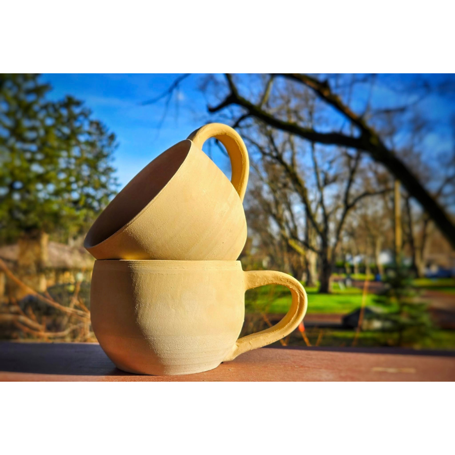Two yellow ceramic mugs stacked on top of each other on a wood surface with a natural landscape in the background