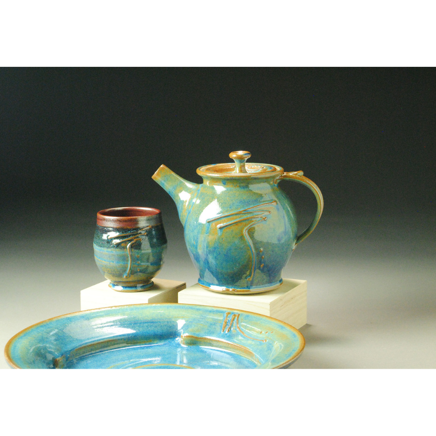 Photo of clay cup, teapot and plate with a light blue glaze
